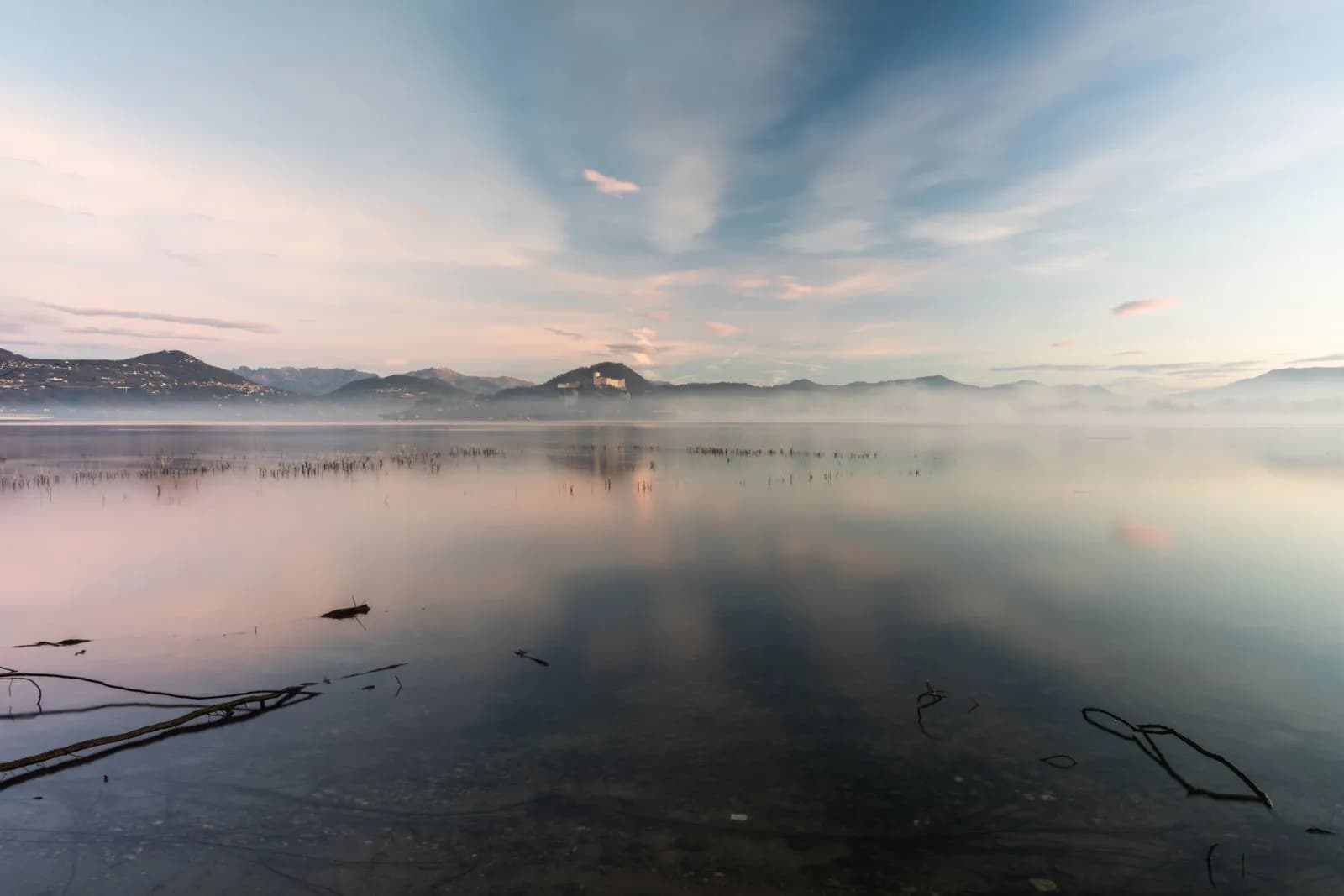 A tranquil misty lake at sunrise with mountains reflected on calm water