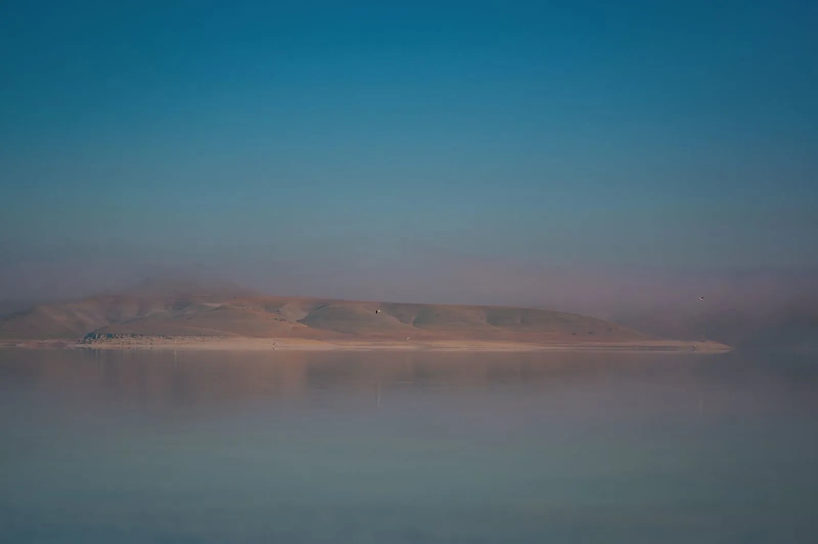 A misty landscape over calm water reflecting mountains at dawn