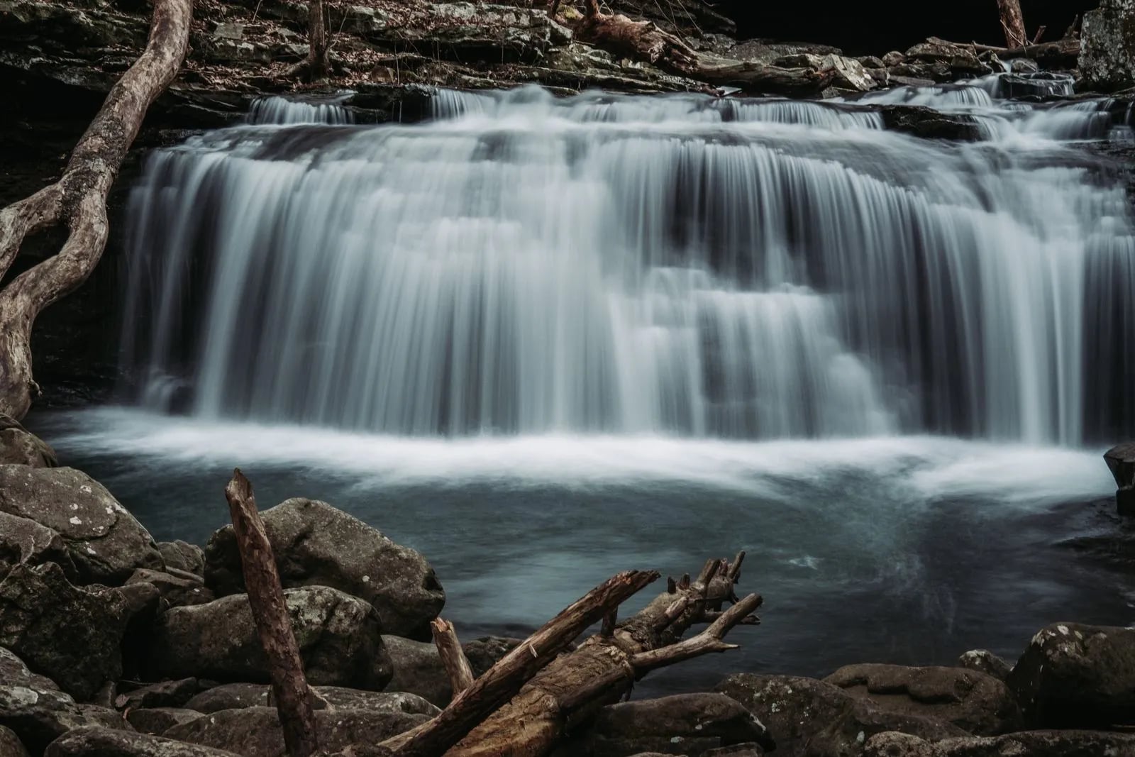 A long-exposure photograph of a waterfall flowing over rocks in a forest